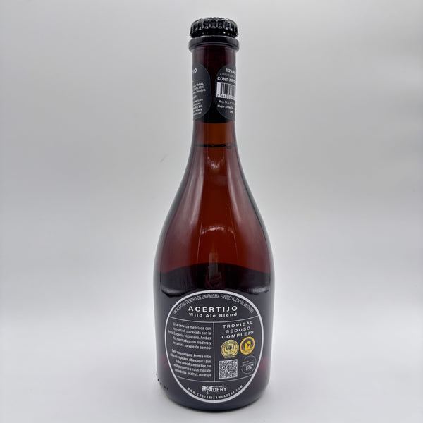 Botella de cerveza artesanal Acertijo Wild Ale Blend con etiqueta ovalada oscura sobre un fondo neutro.