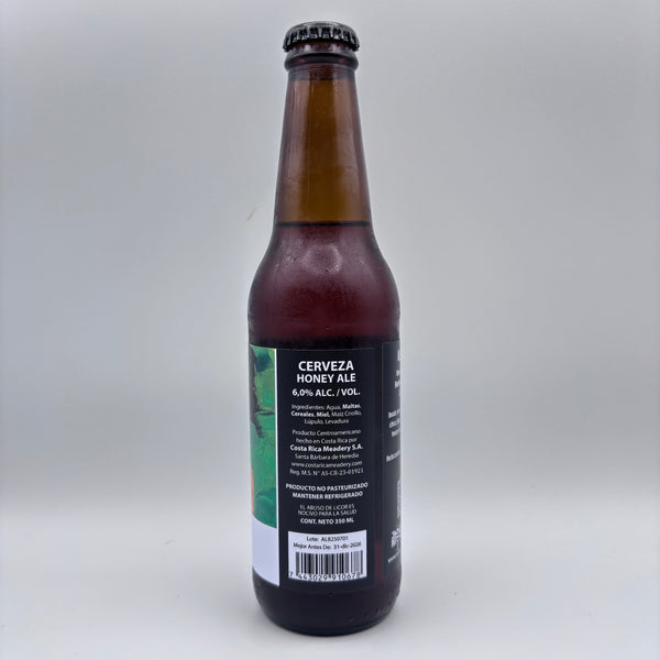 Vista trasera de la botella de Cerveza Honey Ale mostrando el porcentaje de alcohol (6.0% Alc/Vol), información del producto y código de barras sobre un fondo neutro.