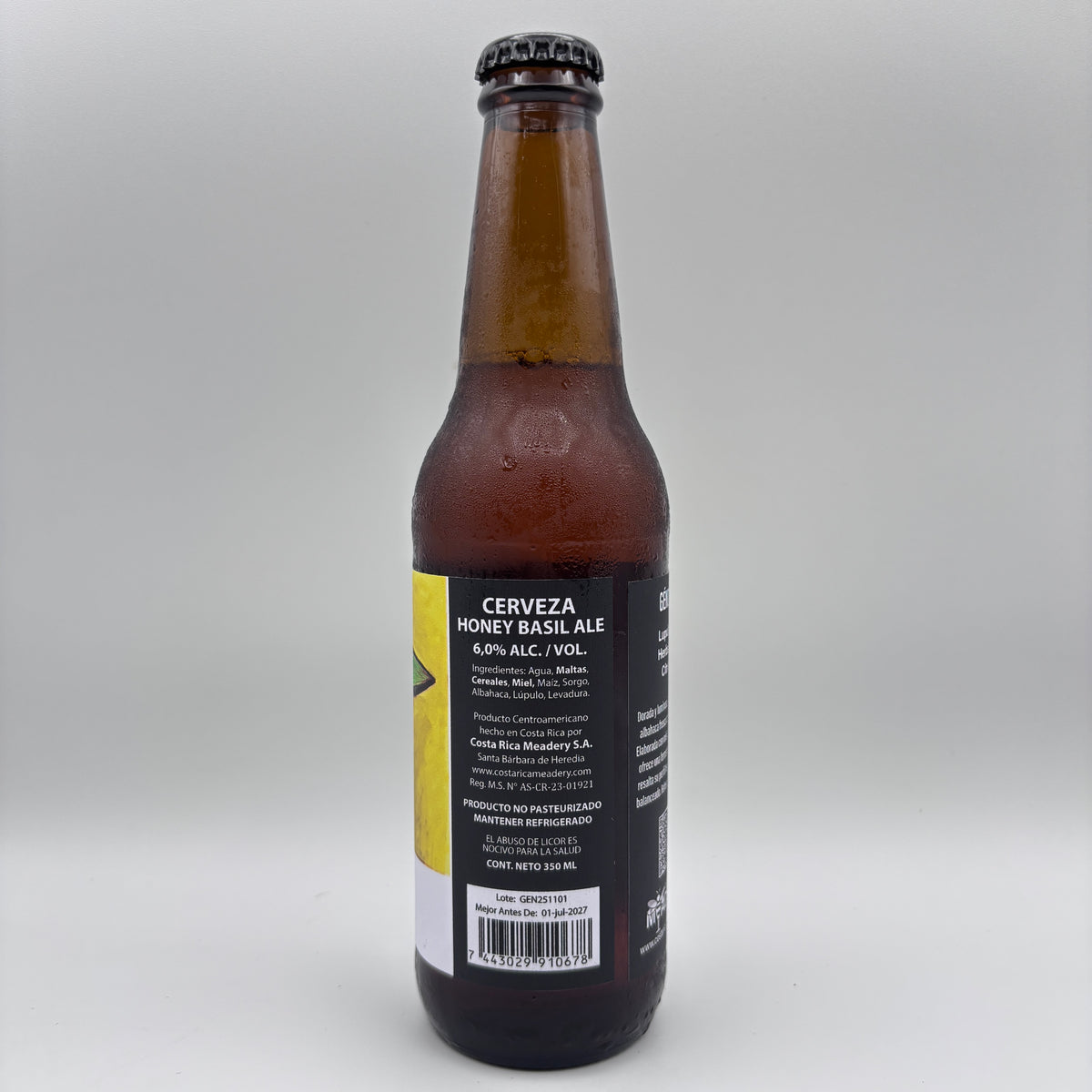 Vista trasera de la botella de Cerveza Honey Basil Ale mostrando el porcentaje de alcohol (6.0% Alc/Vol), información de Costa Rica Meadery y código de barras sobre un fondo neutro.