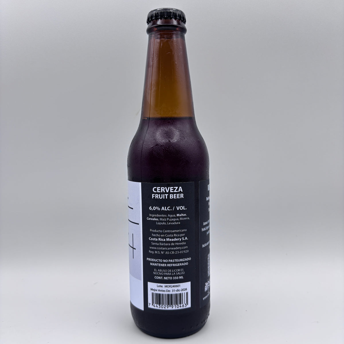 Vista trasera de la botella de Cerveza Morus Fruit Beer mostrando el porcentaje de alcohol (6.0% Alc/Vol), datos de Costa Rica Meadery y código de barras sobre un fondo neutro.