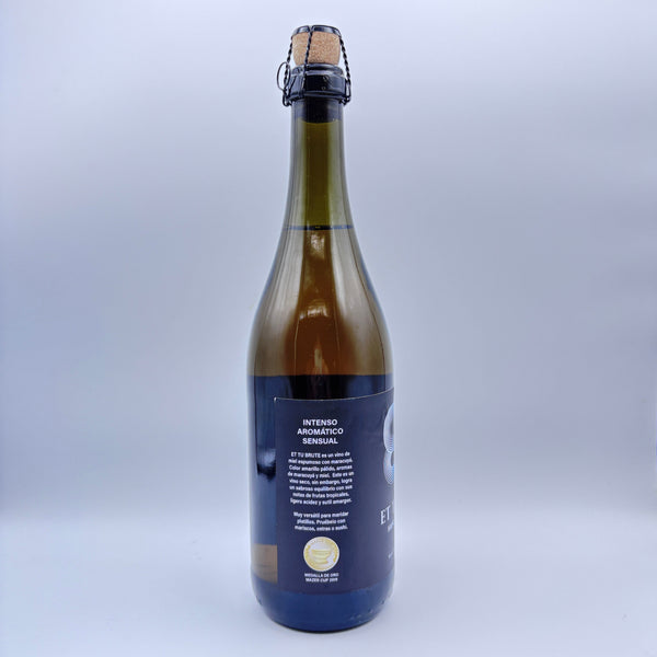 Vista lateral de la botella de hidromiel espumoso Et Tu Brute mostrando en la etiqueta los descriptores Intenso, Aromático y Sensual junto con un sello de medalla de oro sobre un fondo neutro.