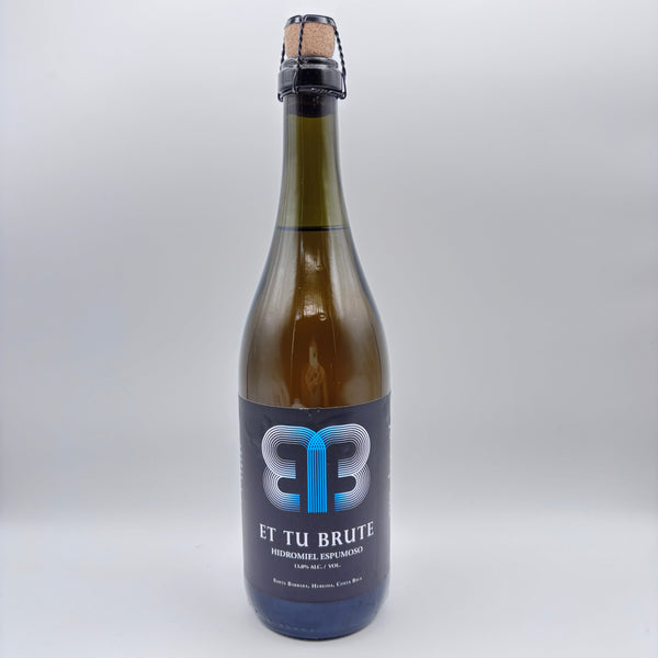 Botella de hidromiel espumoso Et Tu Brute con tapón de corcho y etiqueta oscura con logotipo azul sobre un fondo neutro.