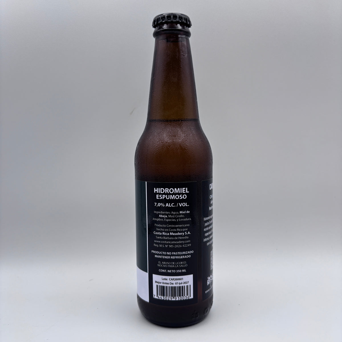Vista trasera de la botella de Hidromiel Espumoso mostrando la contraetiqueta con el porcentaje de alcohol (7.0% Alc/Vol), detalles de Costa Rica Meadery y código de barras sobre un fondo neutro.