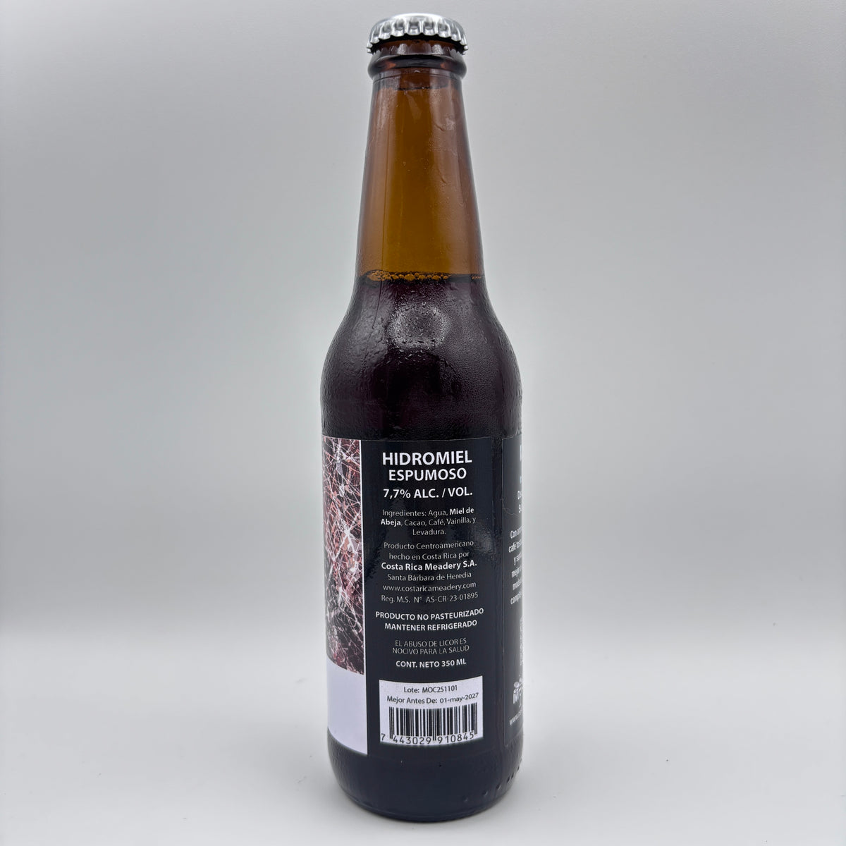 Vista trasera de la botella de Hidromiel Espumoso Möca mostrando el porcentaje de alcohol (7.7% Alc/Vol), detalles de Costa Rica Meadery y código de barras sobre un fondo neutro.