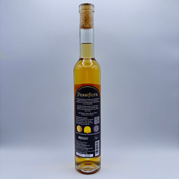 Vista trasera de la botella de hidromiel Passiflora mostrando la contraetiqueta con la descripción del producto, tres sellos de medallas obtenidas, el logo de Costa Rica Meadery y el código de barras sobre un fondo neutro.