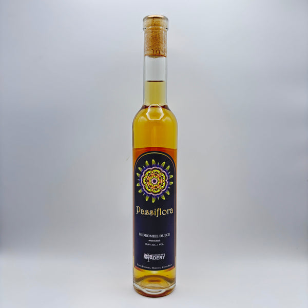 Botella estilizada de hidromiel dulce Passiflora con maracuyá, mostrando una etiqueta oscura con un diseño de mandala multicolor y el logo de Costa Rica Meadery sobre un fondo neutro.