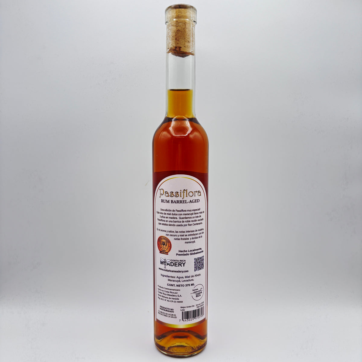 Vista trasera de la botella de hidromiel Passiflora Rum Barrel-Aged mostrando la contraetiqueta con la descripción del producto, sello de premiación, logo de Costa Rica Meadery y código de barras sobre un fondo neutro.