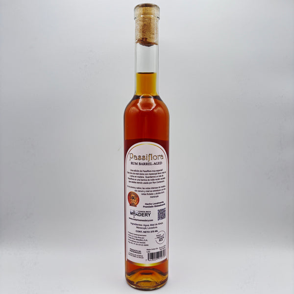Vista trasera de la botella de hidromiel Passiflora Rum Barrel-Aged mostrando la contraetiqueta con la descripción del producto, sello de premiación, logo de Costa Rica Meadery y código de barras sobre un fondo neutro.
