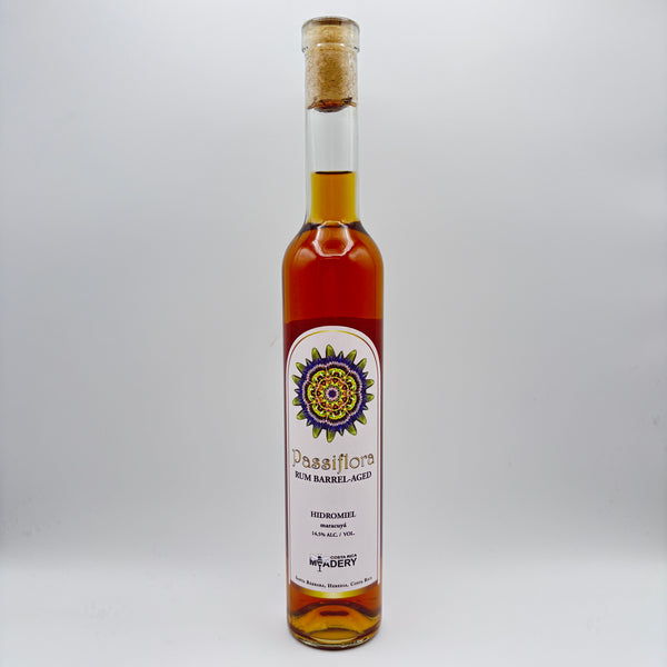 Botella estilizada de hidromiel Passiflora Rum Barrel-Aged con maracuyá, mostrando una etiqueta clara con un diseño mandálico multicolor y el logo de Costa Rica Meadery sobre un fondo neutro.