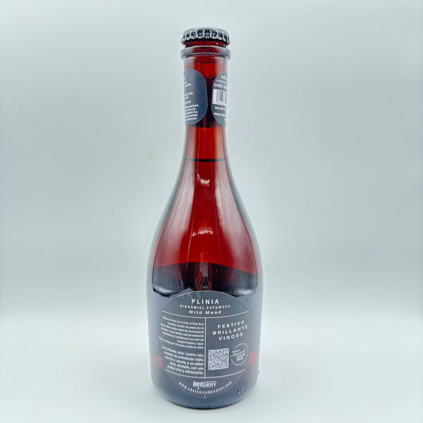 Vista lateral de la botella de Plinia Hidromiel Espumoso Wild Mead mostrando en la etiqueta los descriptores Festivo, Brillante y Vinoso, junto con un código QR y el logo de Costa Rica Meadery sobre un fondo neutro.