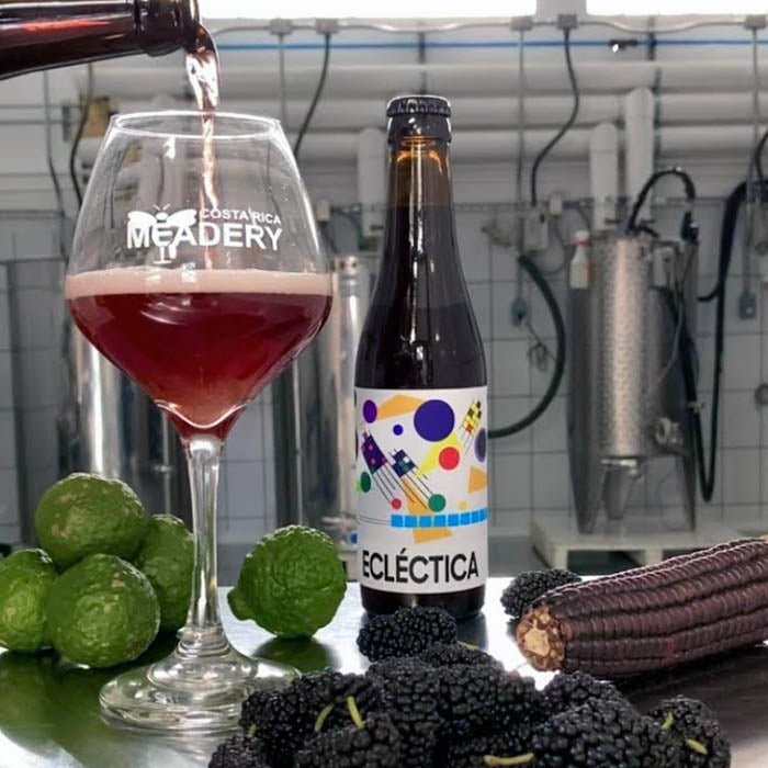 ECLÉCTICA es una cerveza artesanal estilo “wild ale” con morera negra, maíz negro, y miel. - copa y botella